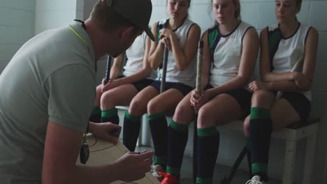 Hockey-coach-explaining-game-plan-with-female-players-in-locker-room