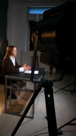 professional soffit standing in the photo studio directed at the woman sitting at desk. female reporter recording a video for blog. vertical video.