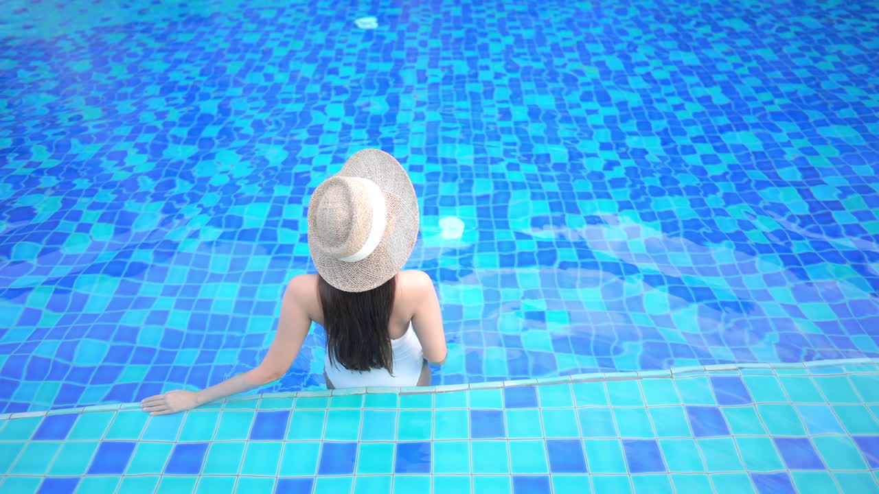 Tampak Belakang Wanita Berpakaian Renang dan Topi Lebar Berdiri Sendiri di Kolam Renang Biru, Bingkai Penuh
