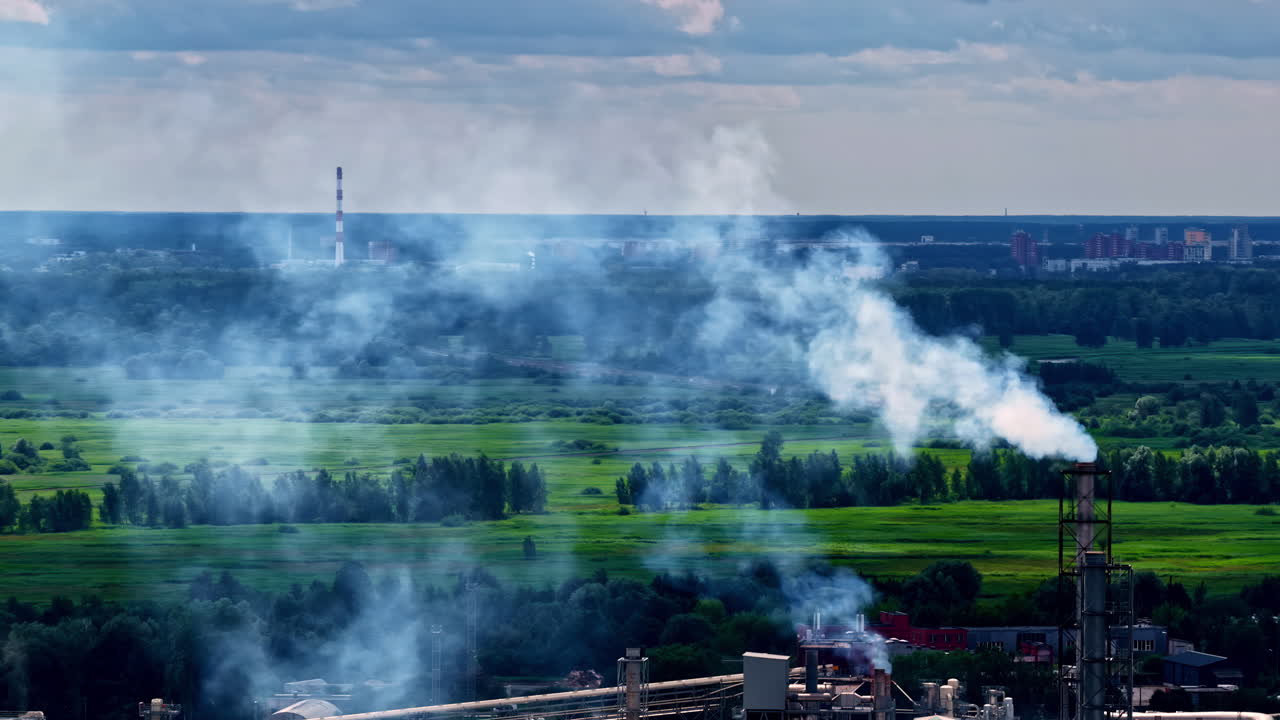 Smoke billows from a factory chimney set against a natural landscape backdrop at dusk