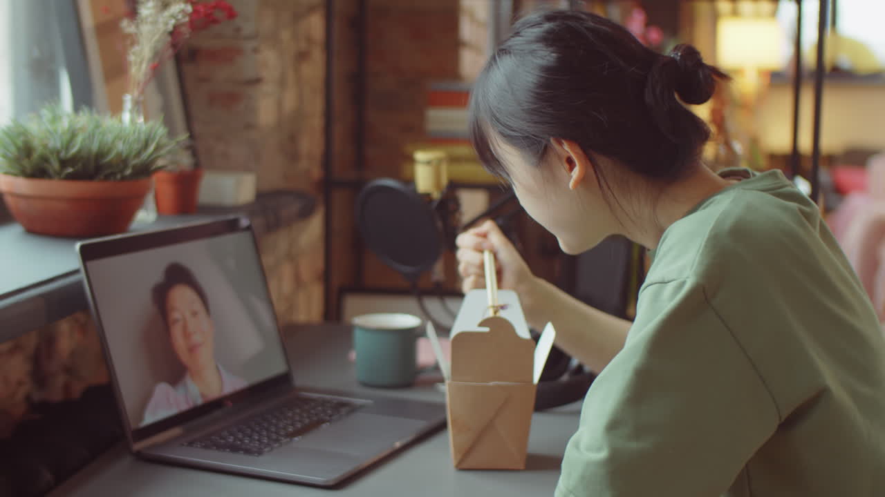 아시안 여성이 집에서 먹고 비디오 통화를 하고 있습니다.