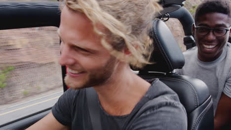 group of young friends having fun in open top hire car on summer vacation