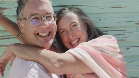 retrato de una feliz pareja caucásica mayor abrazándose y riendo junto a una pared de madera, en cámara lenta