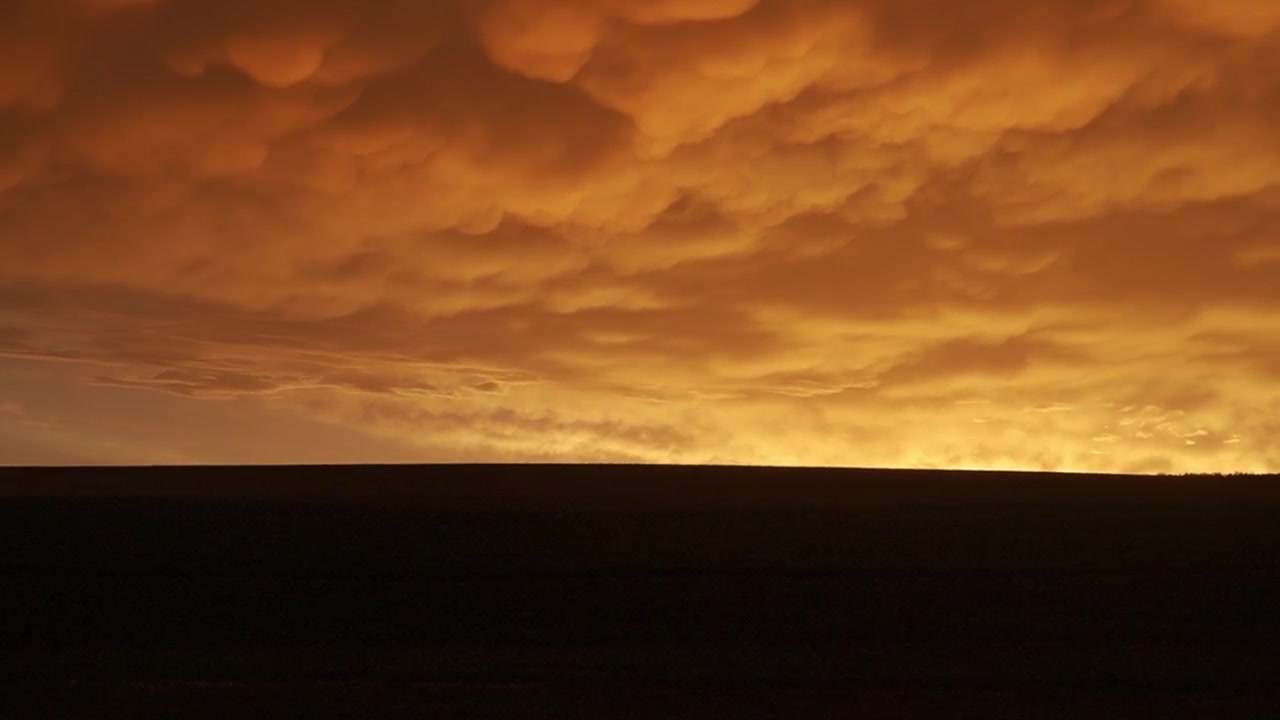 Dramatische Mammatuswolkenformation bei Sonnenuntergang mit leuchtenden gold-orangen Farben. Erstaunliches atmosphärisches Wetterphänomen über einem dunklen Horizont