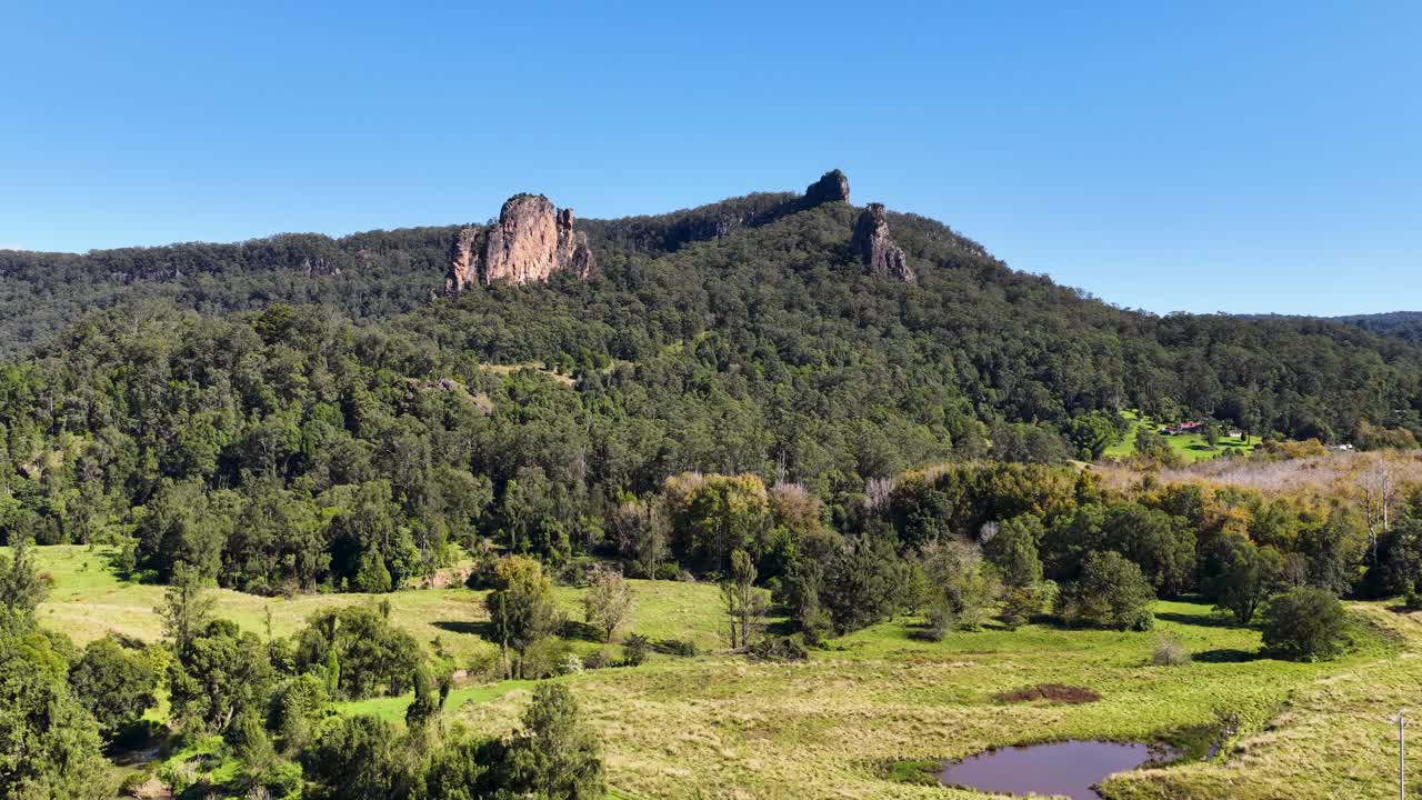 Panoramic view of Nimbin Rocks under clear blue skies, showcasing lush greenery and rugged terrain