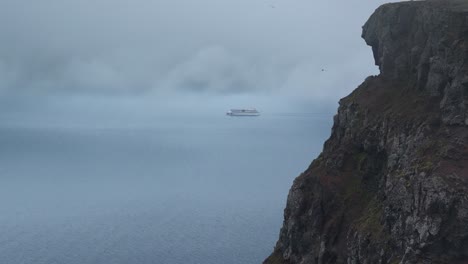 aerial wide shot of cruise ship on fjord water during cloudy day on iceland island with steep cliffs