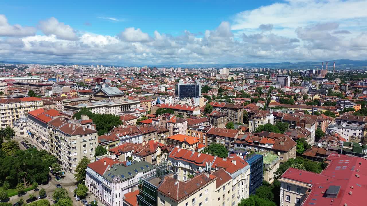 Reveal aerial shot of Sofia, Bulgaria. Drone flying over the city center, facing northeast, a sunny summer day, with beautiful white clouds in the blue sky. An East European capital city