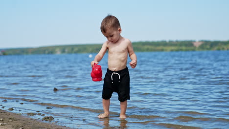 beautiful caucasian toddler playing in the beach. kid carries a watering can filled with water from river.
