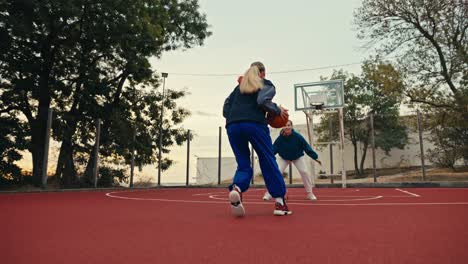 Shot-from-below-a-blonde-girl-in-a-sports-uniform-runs-along-a-red-street-basketball-court-and-throws-the-ball-into-a-basketball-hoop-in-the-morning