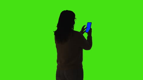 rear view of silhouetted woman using blue screen mobile phone standing against green screen background