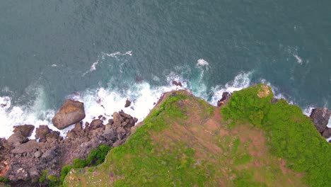 overhead drone shot of cliffs with a rocky base crushed by big waves