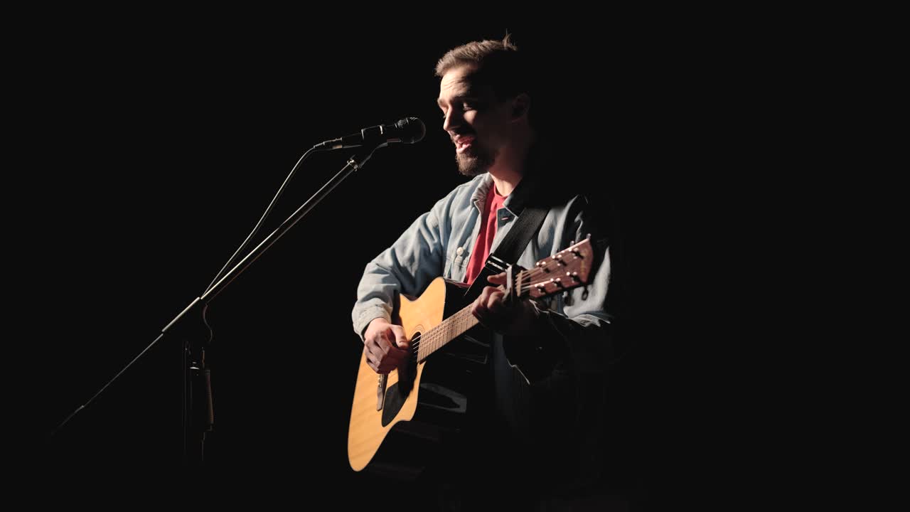 A musician is playing guitar on a large stage with audience members holding flashlights in the background. The auditorium is filled with beautiful flashing lights.
