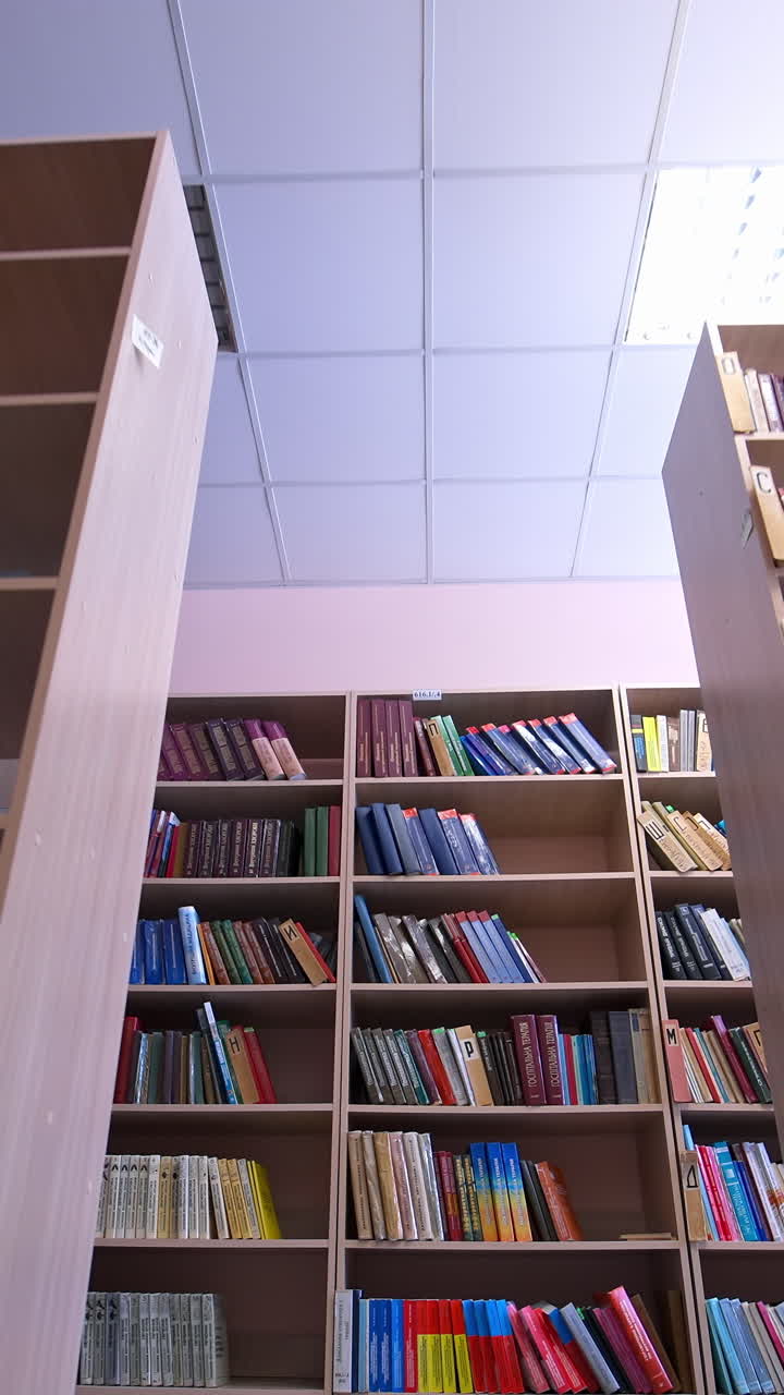 Library books stacked on shelves. Rows of bookcases with books in the library. Education, school or university learning concept. Camera moves back. Vertical video