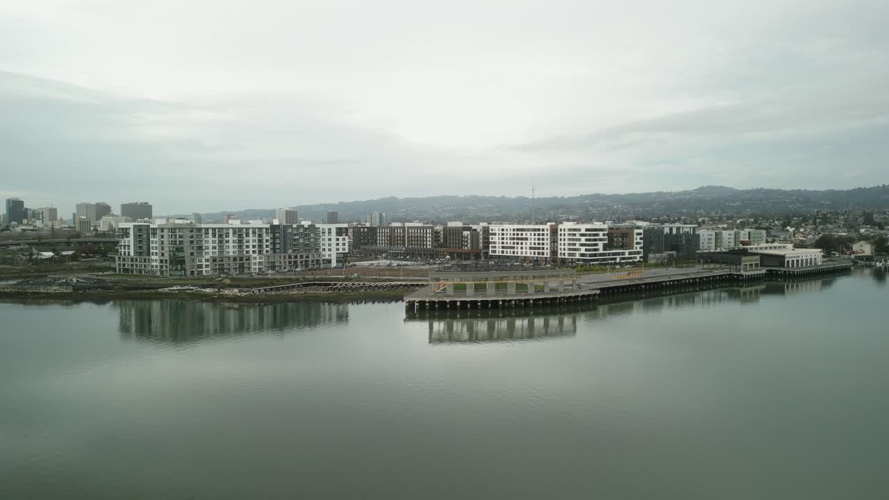 Aerial drone view of Jack London Square at sunset, with glowing city lights reflecting off the water and vibrant activity below.