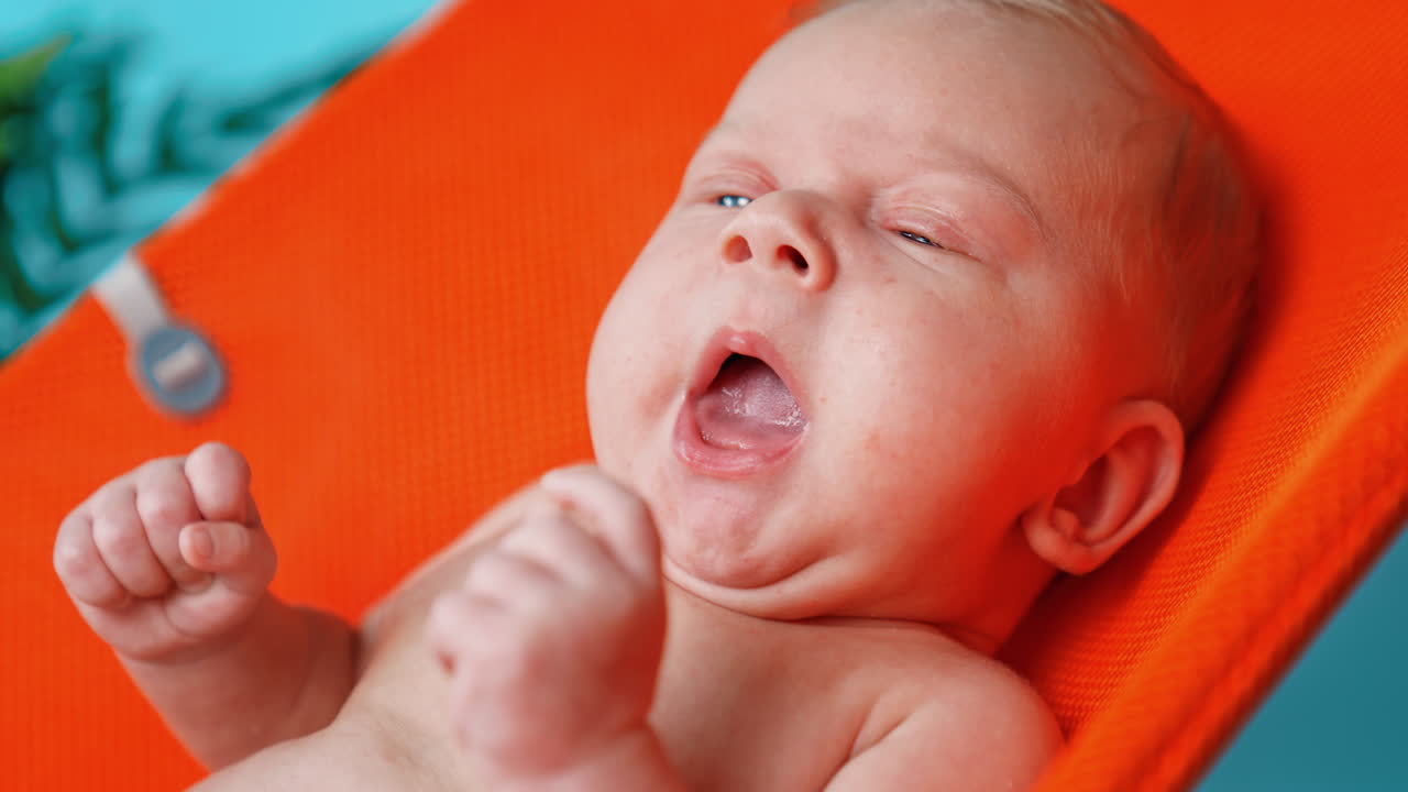 Newborn boy with blond hair and blue eyes. Close up portrait. Little baby is yawning.