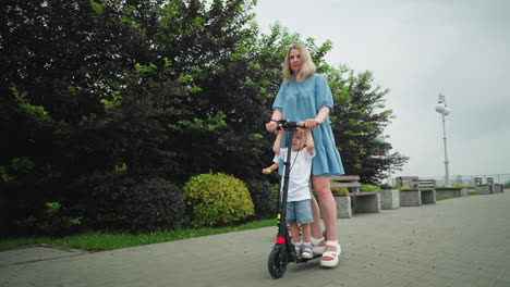 a mother rides a scooter with her younger child on a curved path, while her older child rides independently behind them