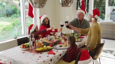 Happy-caucasian-multi-generation-family-wearing-santa-hats,-having-christmas-meal,-making-toast