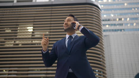 happy businessman talking on phone standing by office building, reporting good news