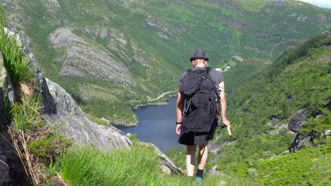 man complete mountain fishing trip and proceeds downhill towards bergsdalen norway while holding fishing rod in hs hand