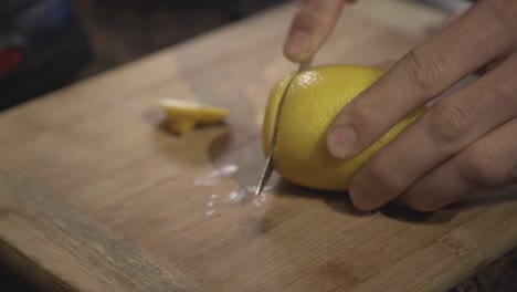 a person hands slowly cutting a fresh lemon on a wooden board - close up shot