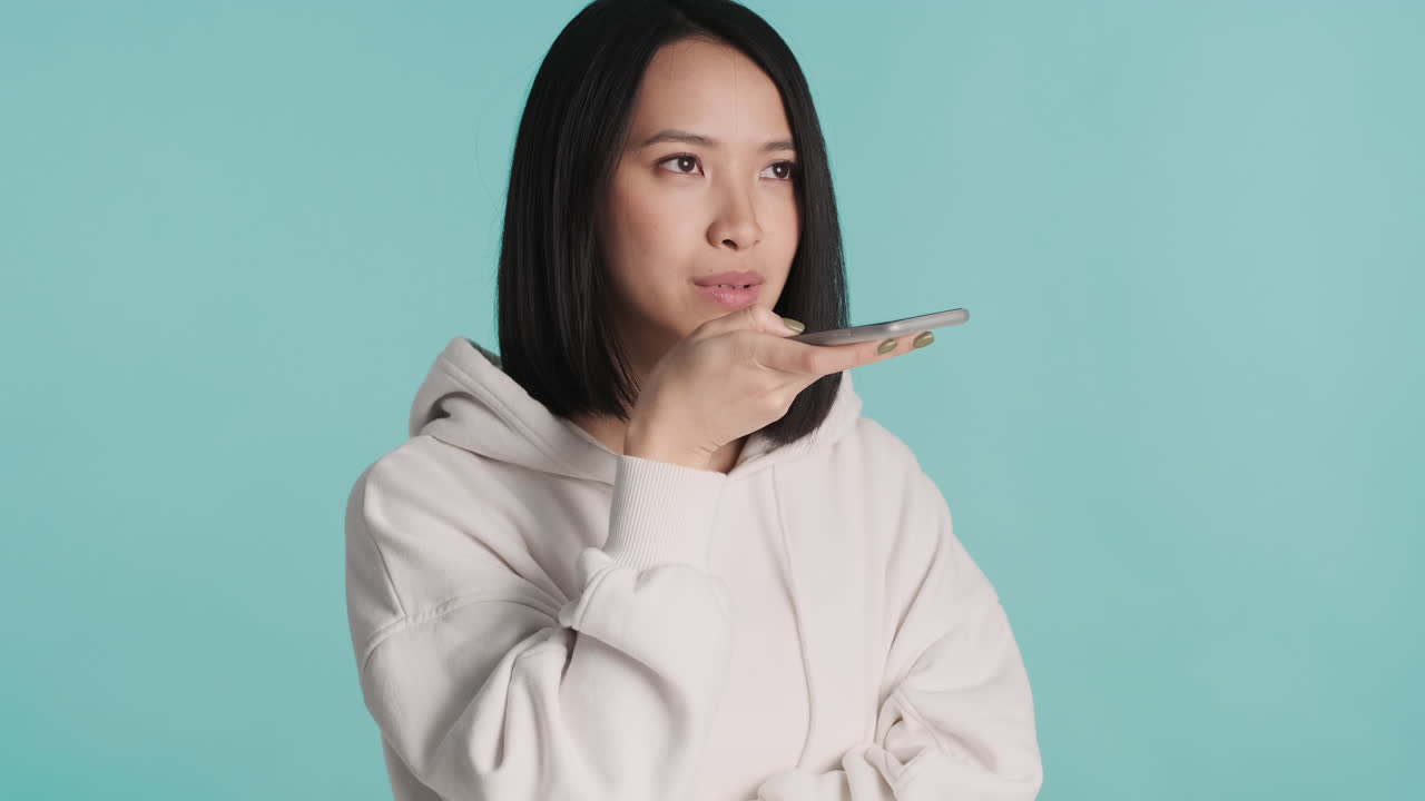 아시아 여성이 스마트폰으로 음성 메시지를 녹음하고 있습니다.