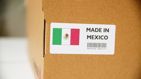 manos aplicando la etiqueta de la bandera hecha en méxico en una caja de cartón de envío con productos