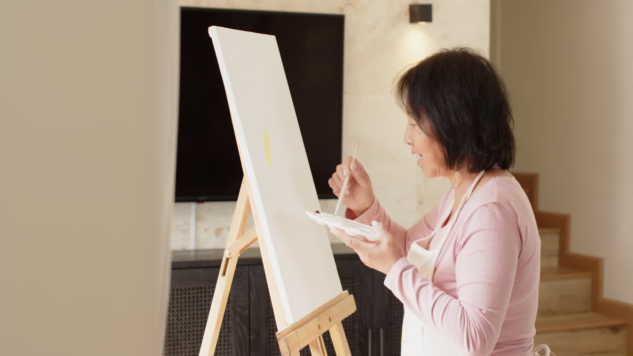 Senior Asian woman painting on canvas at home, enjoying creative solitude