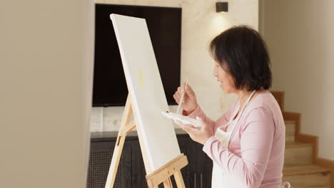senior asian woman painting on canvas at home, enjoying creative solitude