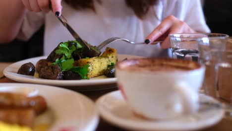 Close-up-in-slow-motion,-lady's-hand-picking-up-mushroom-on-her-plate-with-knife-and-fork-in-a-cafe