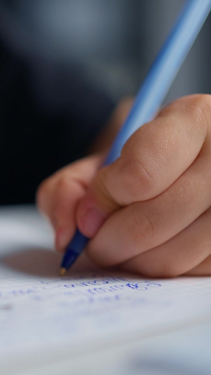 Primo Piano della Mano di un Bambino che Scrive con una Penna Blu su Carta