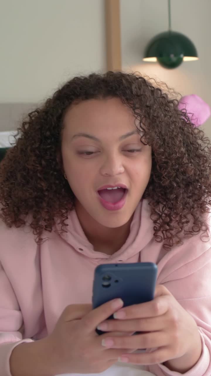 Vertical video: Reacting to text, woman reading, speaking in bed, blue phone, pink hoodie and socks