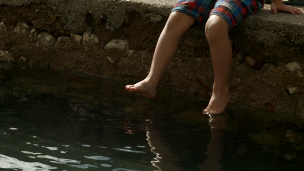 Boy Sitting on a Pier with Feet in Water