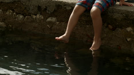 boy sitting on a pier with feet in water