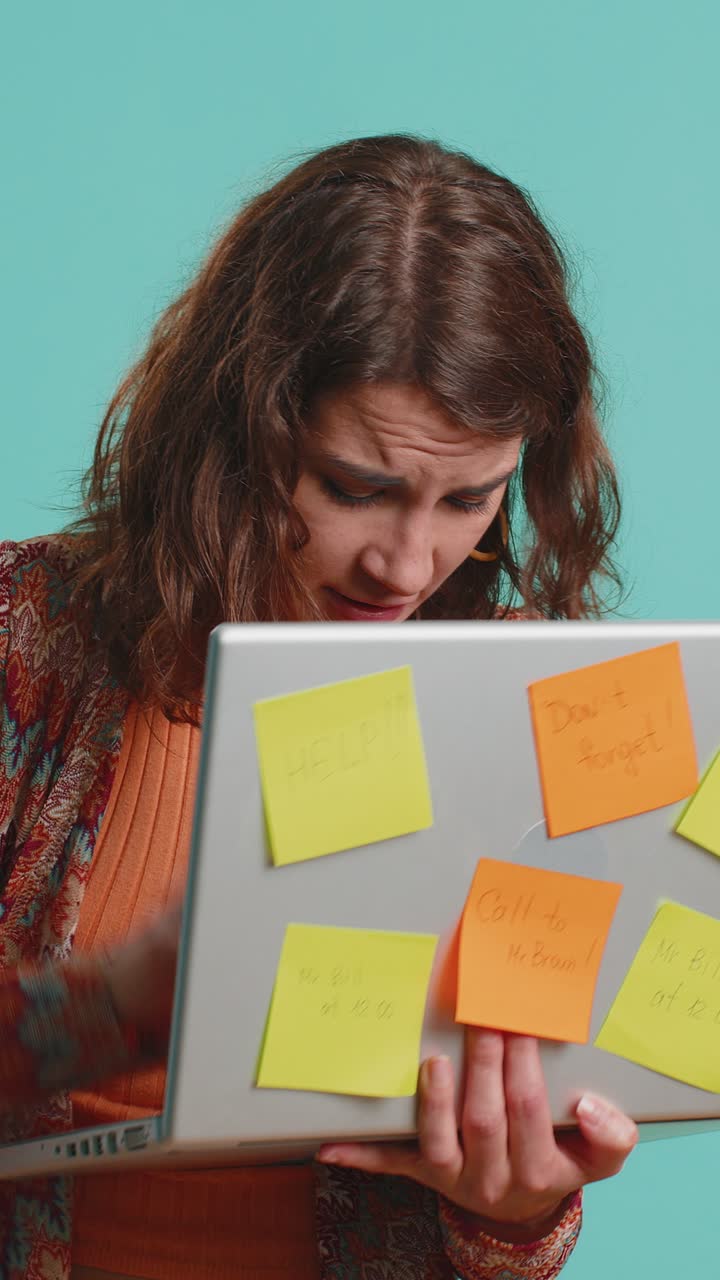 Donna freelance esausta con appunti adesivi incollati usa il portatile confusa dal grande carico di lavoro di routine