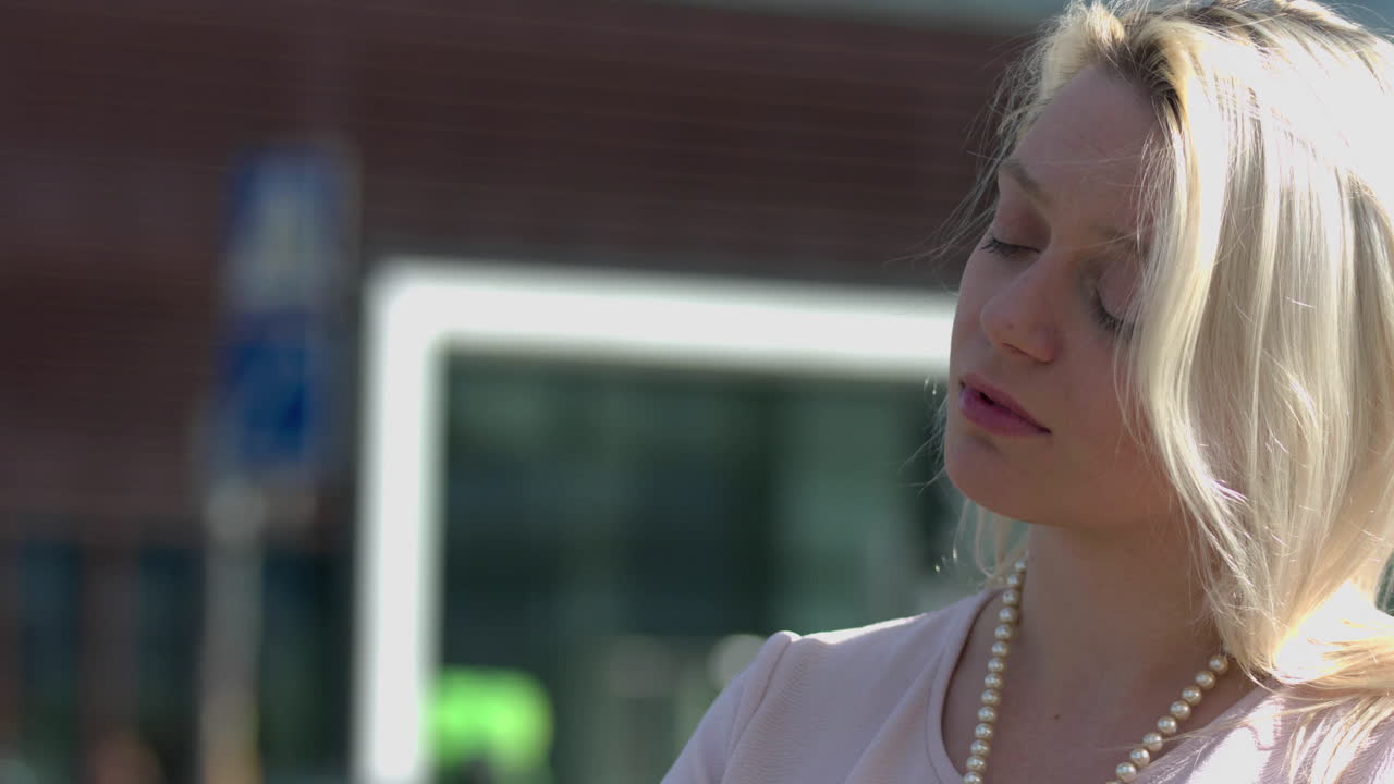 молодая женщина стоит на улице на оживленной дороге в течение рабочего дня, за ней интенсивное движение транспорта