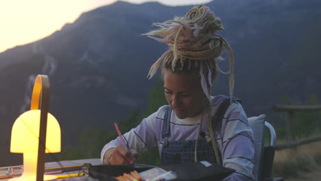 hippie-mädchen mit blonden dreadlocks, tief in gedanken versunken, zeichnet oder schreibt im freien