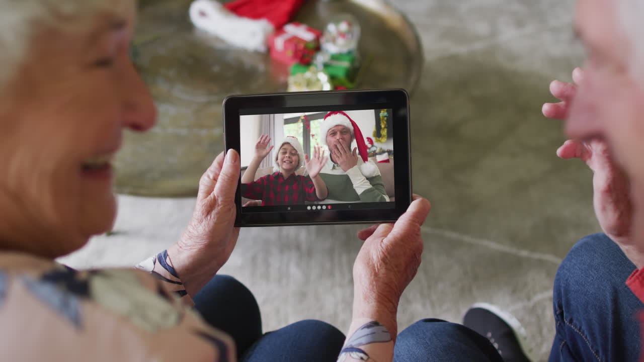 Coppia anziana caucasica che usa un tablet per una videochiamata di Natale con una famiglia felice sullo schermo