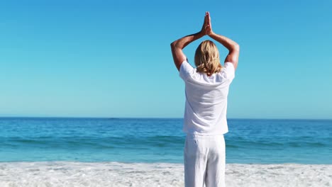 Rear-view-of-man-performing-yoga-at-beach