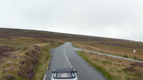 Forwards-flyover-historic-sports-car-driving-on-curvy-road-in-autumn-countryside.-Grasslands-under-overcast-sky.-Ireland