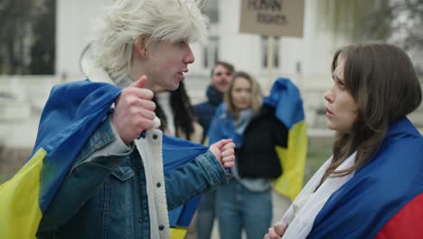 kaukazyjska kobieta z rosyjską flagą kłóci się z kaukazyjskim mężczyzną z ukraińską flagą na demonstracji ulicznej.