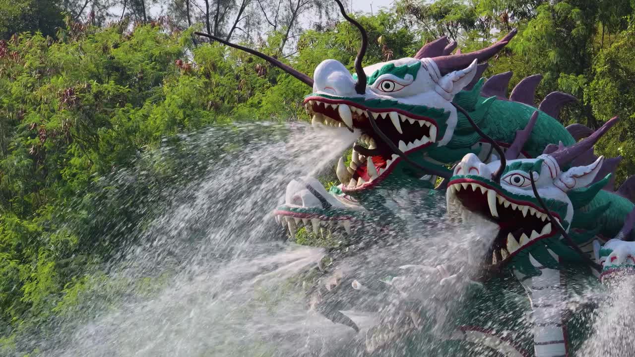 A vibrant dragon sculpture sprays water in a lush, green setting, creating a dynamic and captivating scene.