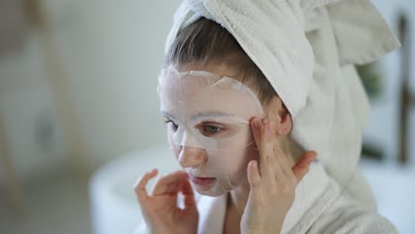 Close-up-of-a-young-domestic-woman-apply-tissue-face-mask-for-skin-care-in-the-bathroom