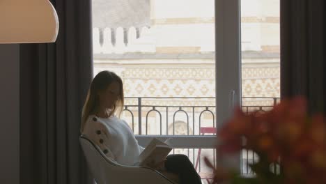 beautiful jung woman is leafing through a book and enjoys the view out of a big window