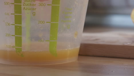 freshly squeezed orange juice dripping into a plastic measuring cup - extreme close up, slow motion