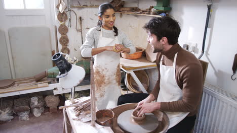 female teacher helping man sitting at wheel in pottery class