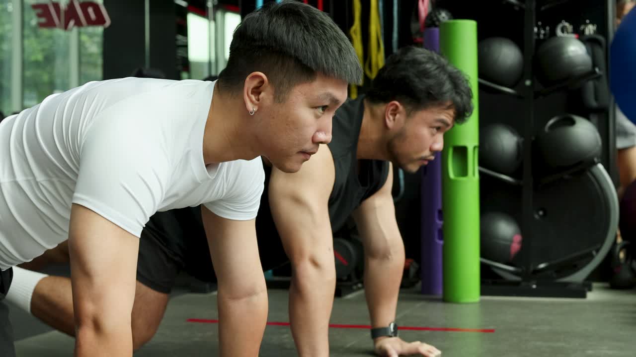Two men perform planks on gym mats, showcasing strength and focus in a fitness studio