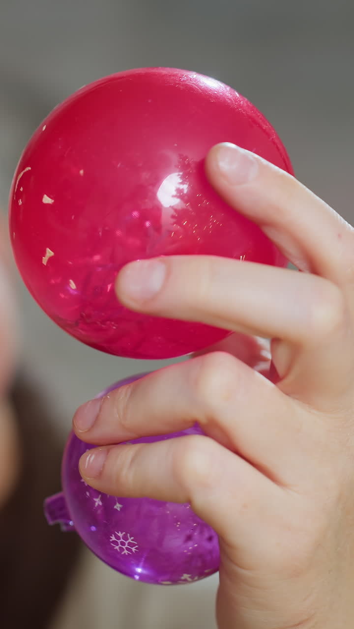 Белый ребенок держит разноцветный мячик-антистресс, крупный план маленьких ручек, изучающих глянцевые красные и фиолетовые сенсорные игрушки, сжимающих и вращающих их, чтобы изучить текстуру и блеск, на кадрах показан тестер игрушек, крафт