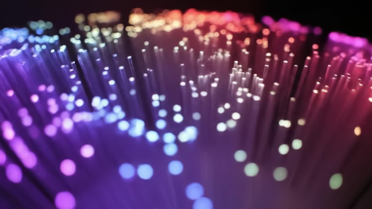 Bright, colorful fiber optic strands pulse and shimmer in various hues, creating a stunning light show in a dark environment. This captivating display enchants viewers with its beauty.
