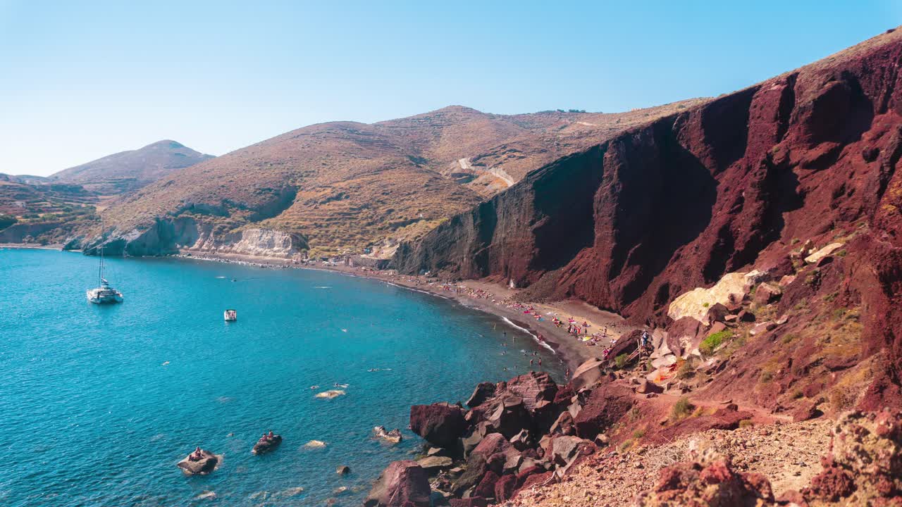 timelapse de una bahía en una isla griega durante el verano con turistas en un sendero y playa y barcos
