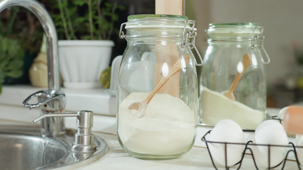 Close up of lady standing in bright kitchen gently drying wet hands with soft towel after washing, surrounded by clean surfaces, colander on counter, and reflection of someone walking in on the mirror